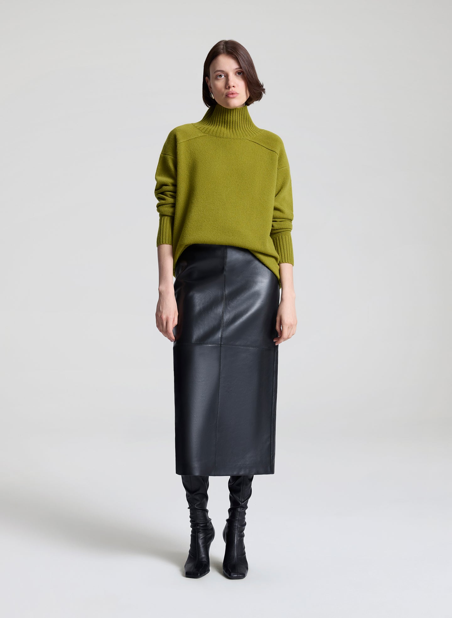 Woman wearing a green sweater and black leather skirt against a white background