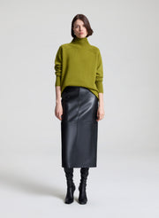 Woman wearing a green sweater and black leather skirt against a white background