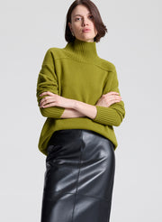 Woman wearing a green sweater and black leather skirt against a white background