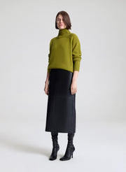 Woman wearing a green sweater and black leather skirt against a white background