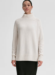 Person wearing a beige sweater on a plain background