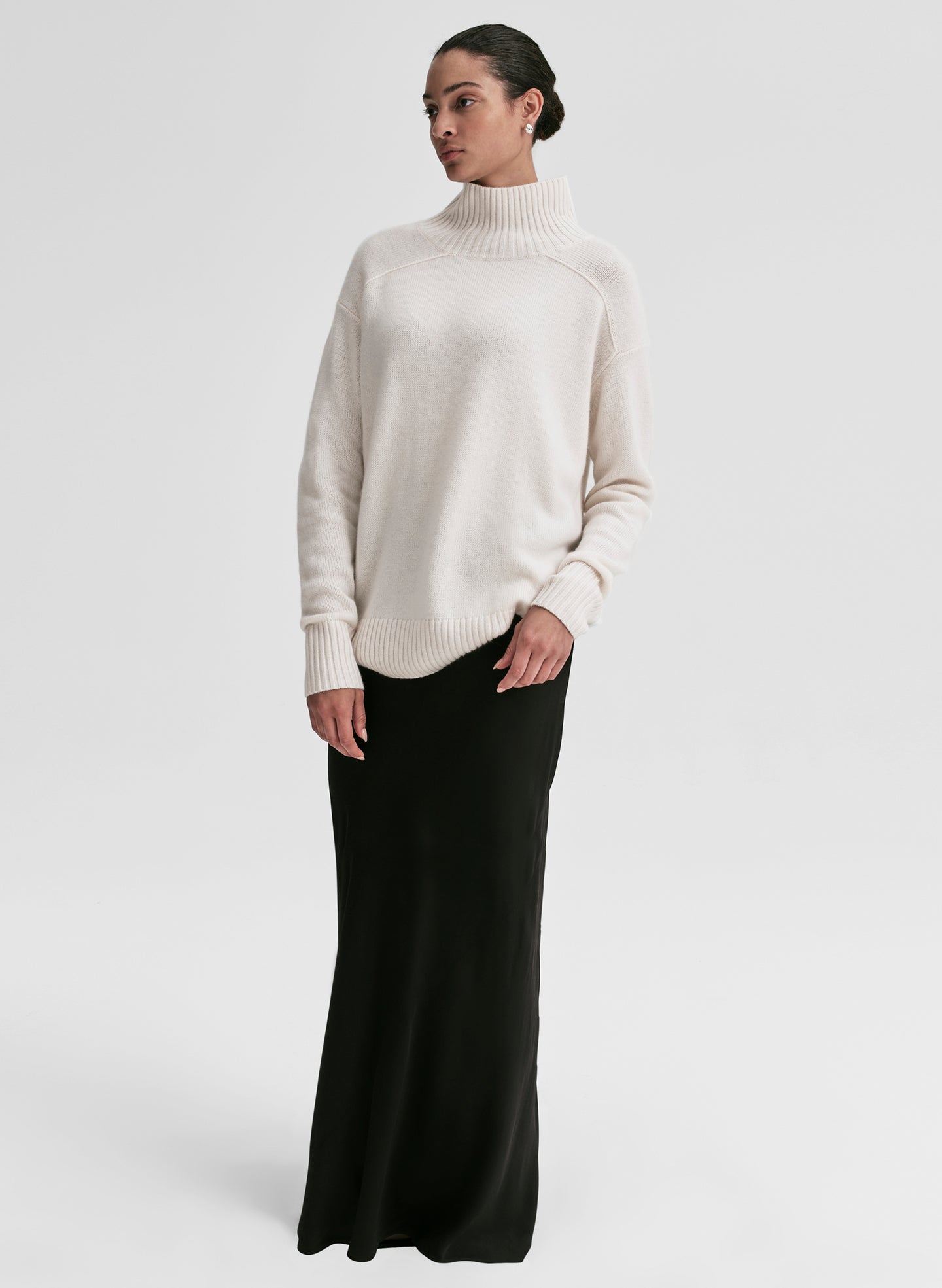 Woman wearing a white turtleneck sweater and black skirt on a light gray background