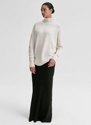 Woman wearing a white turtleneck sweater and black skirt on a light gray background