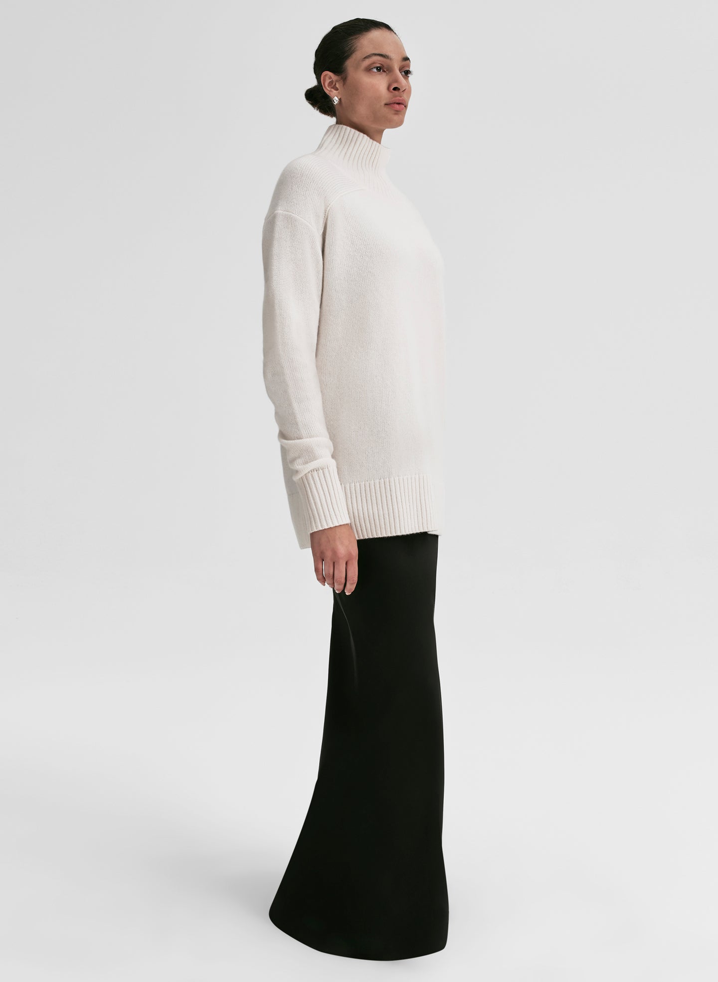 Person wearing a white turtleneck sweater and black skirt on a light gray background
