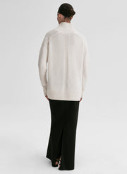 Person wearing a white sweater and black pants on a light gray background