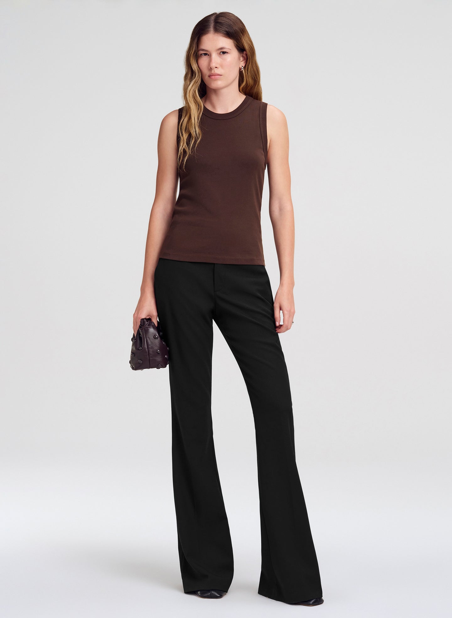 Woman wearing a brown sleeveless top and black pants on a white background