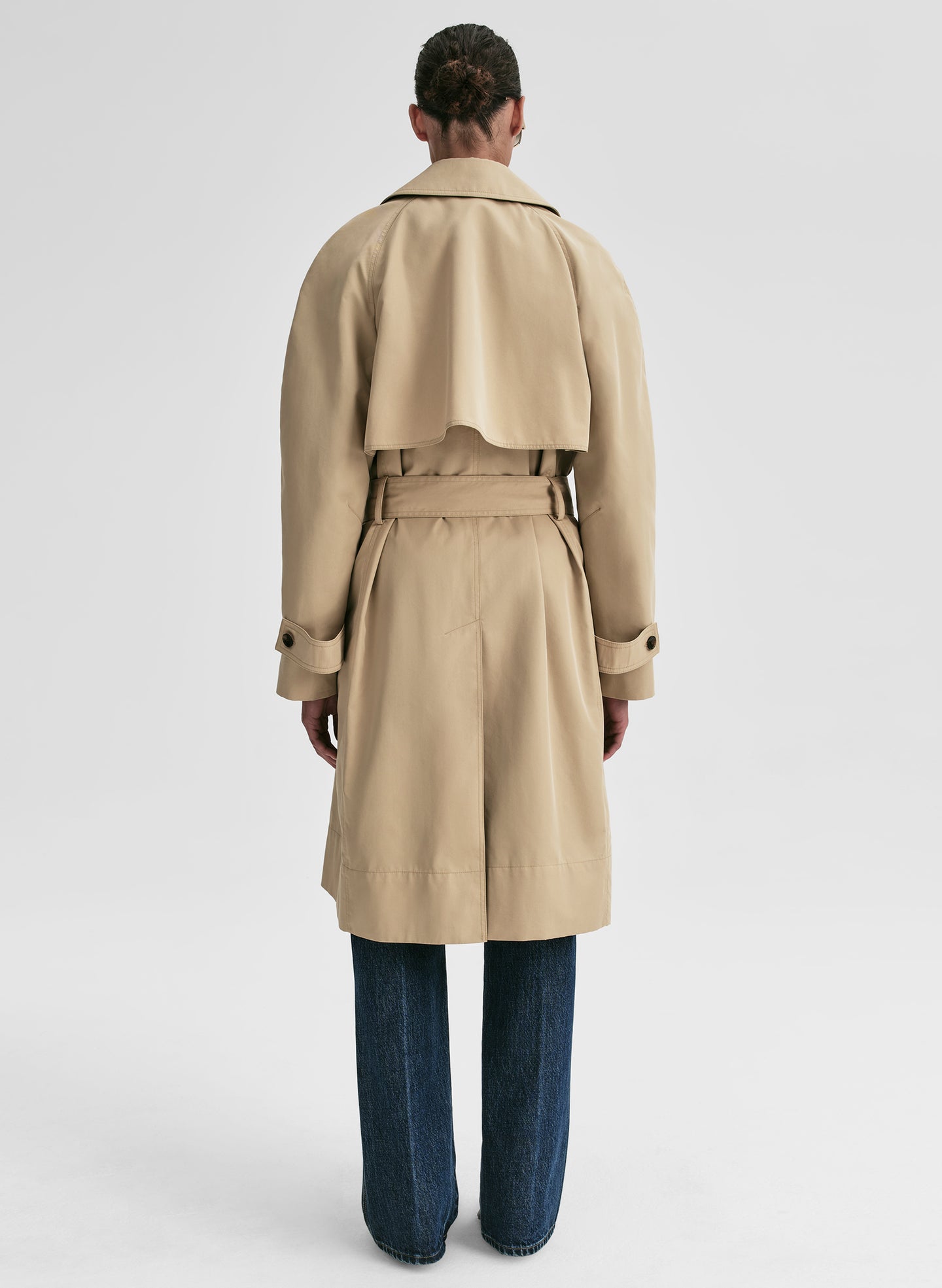 Person wearing a beige trench coat on a light gray background
