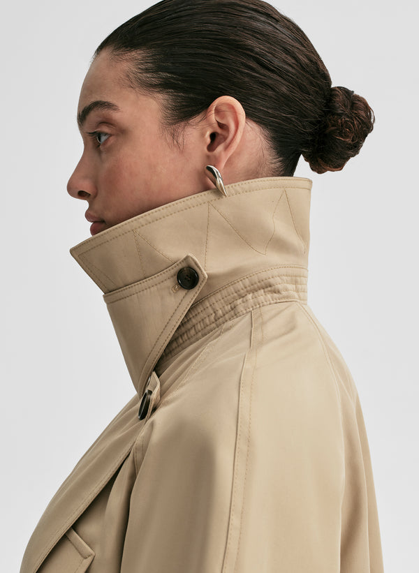 Woman wearing a beige trench coat against a plain background