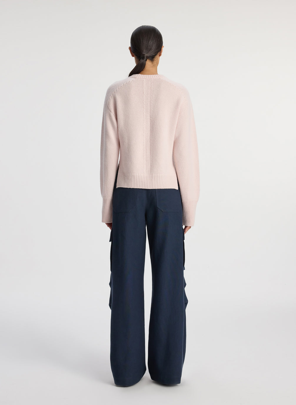 back view of woman wearing pink sweater and navy blue satin cargo pants