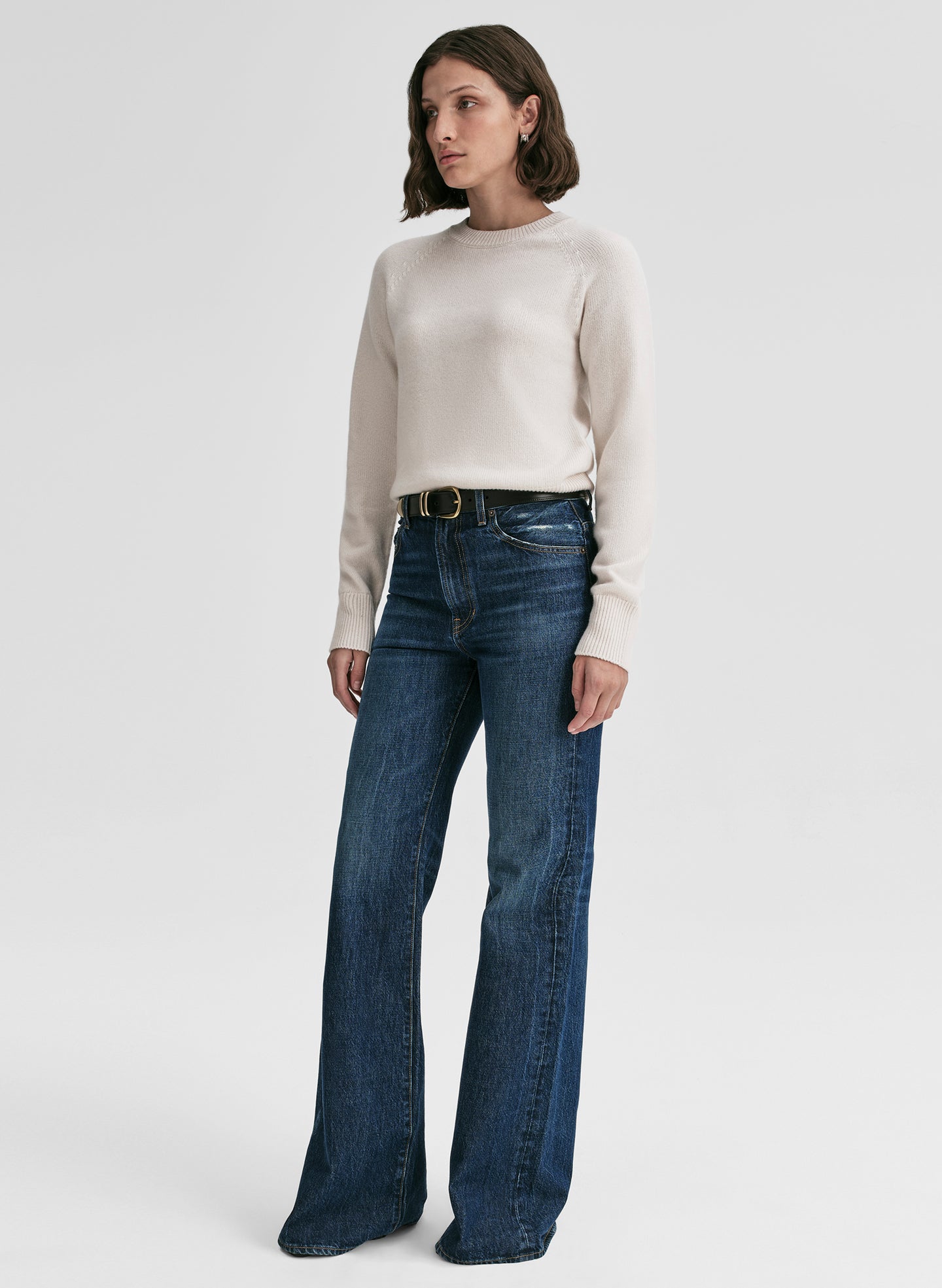 Woman wearing a white sweater and blue jeans on a white background