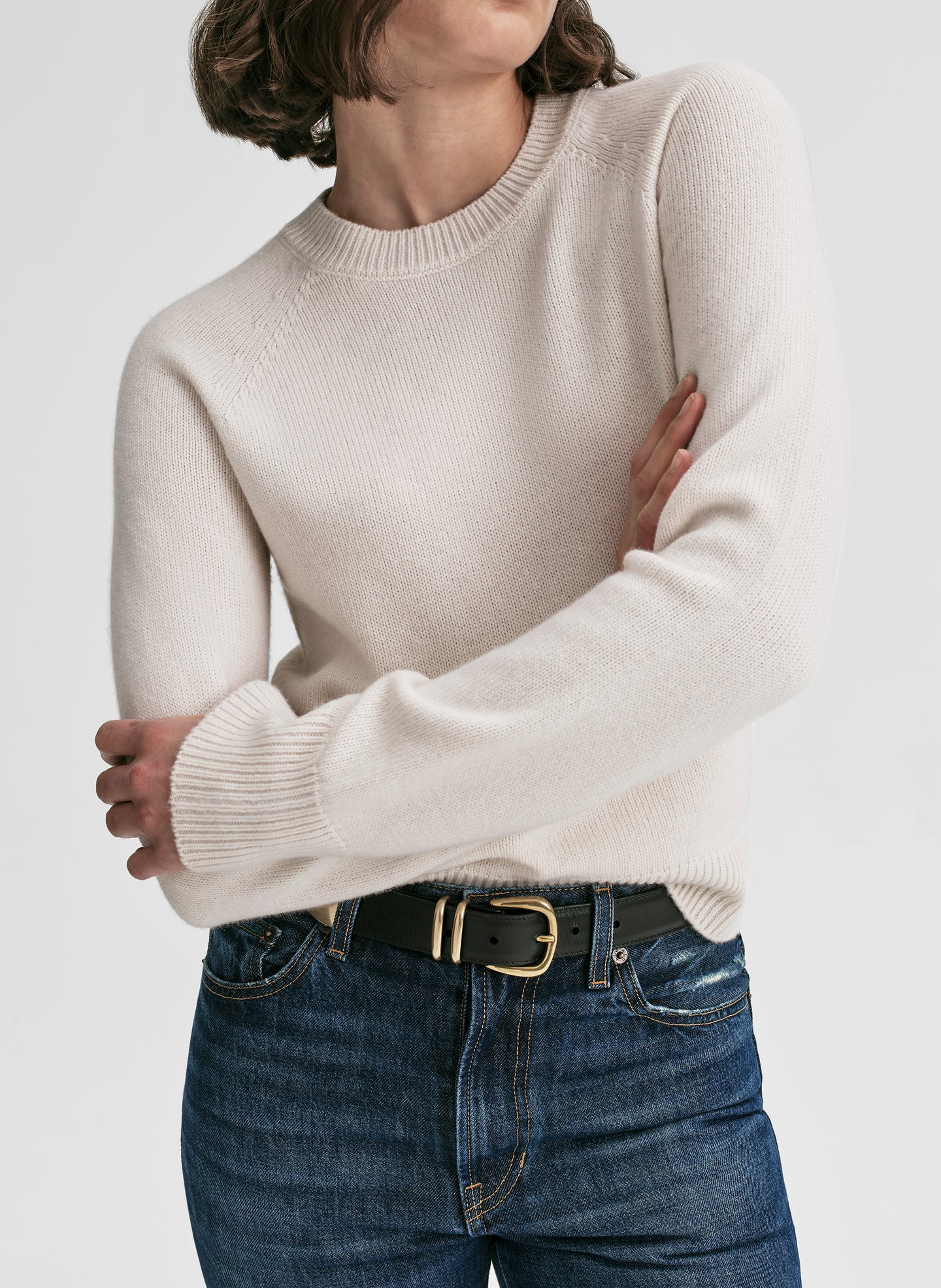 Person wearing a beige sweater and blue jeans with a white background