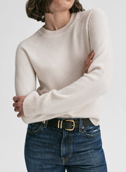 Person wearing a beige sweater and blue jeans with a white background