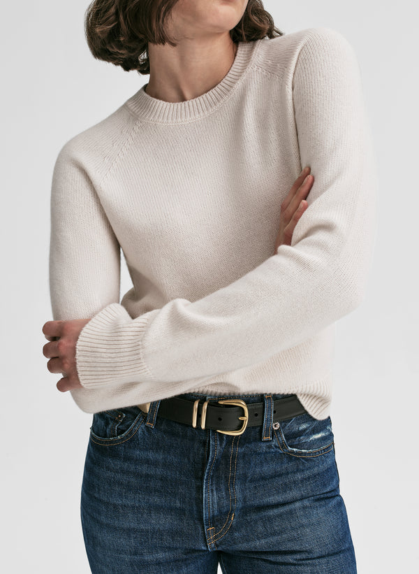Person wearing a beige sweater and blue jeans with a white background