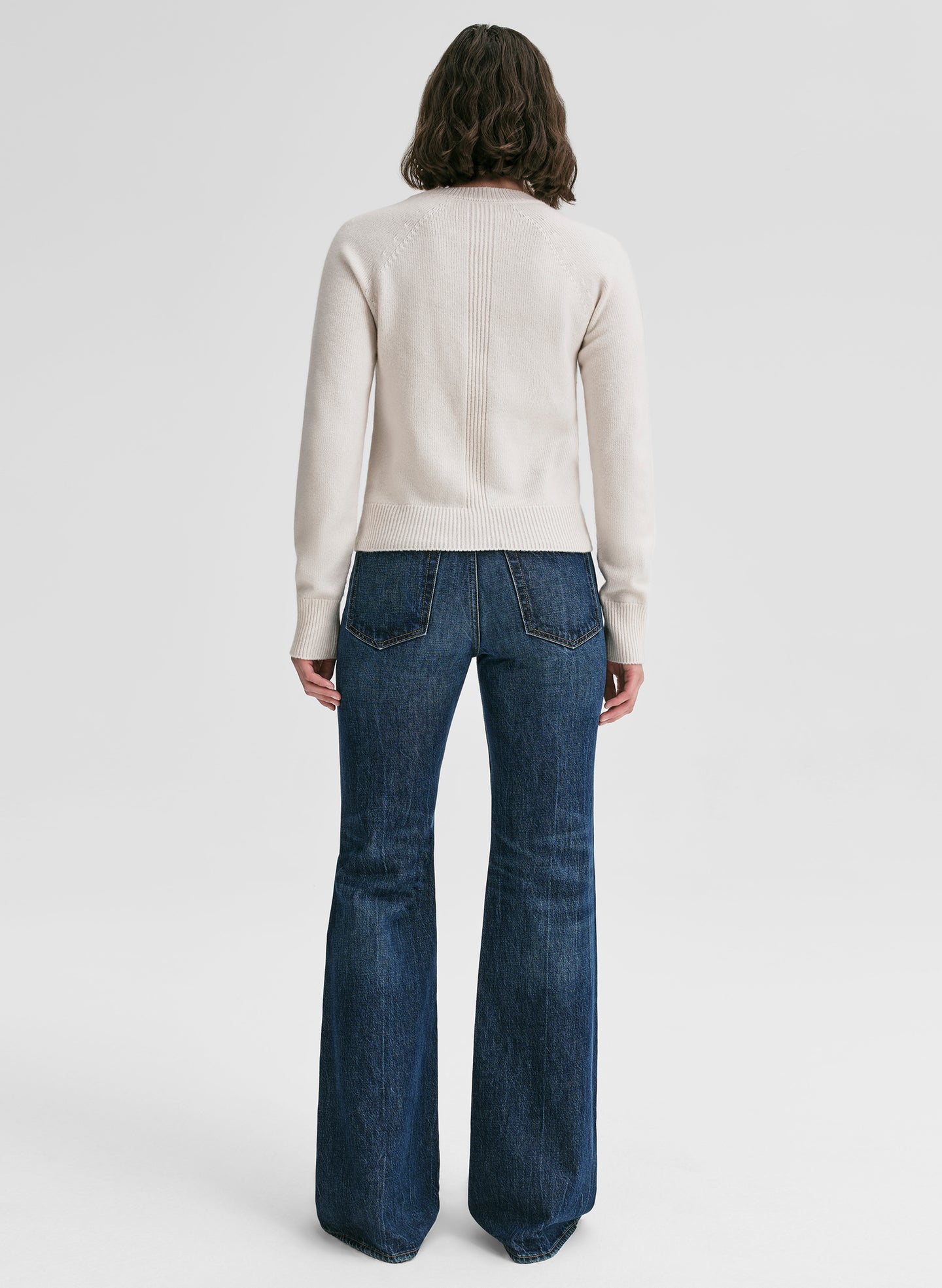 Person wearing a cream sweater and blue jeans on a white background