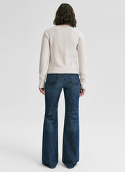 Person wearing a cream sweater and blue jeans on a white background