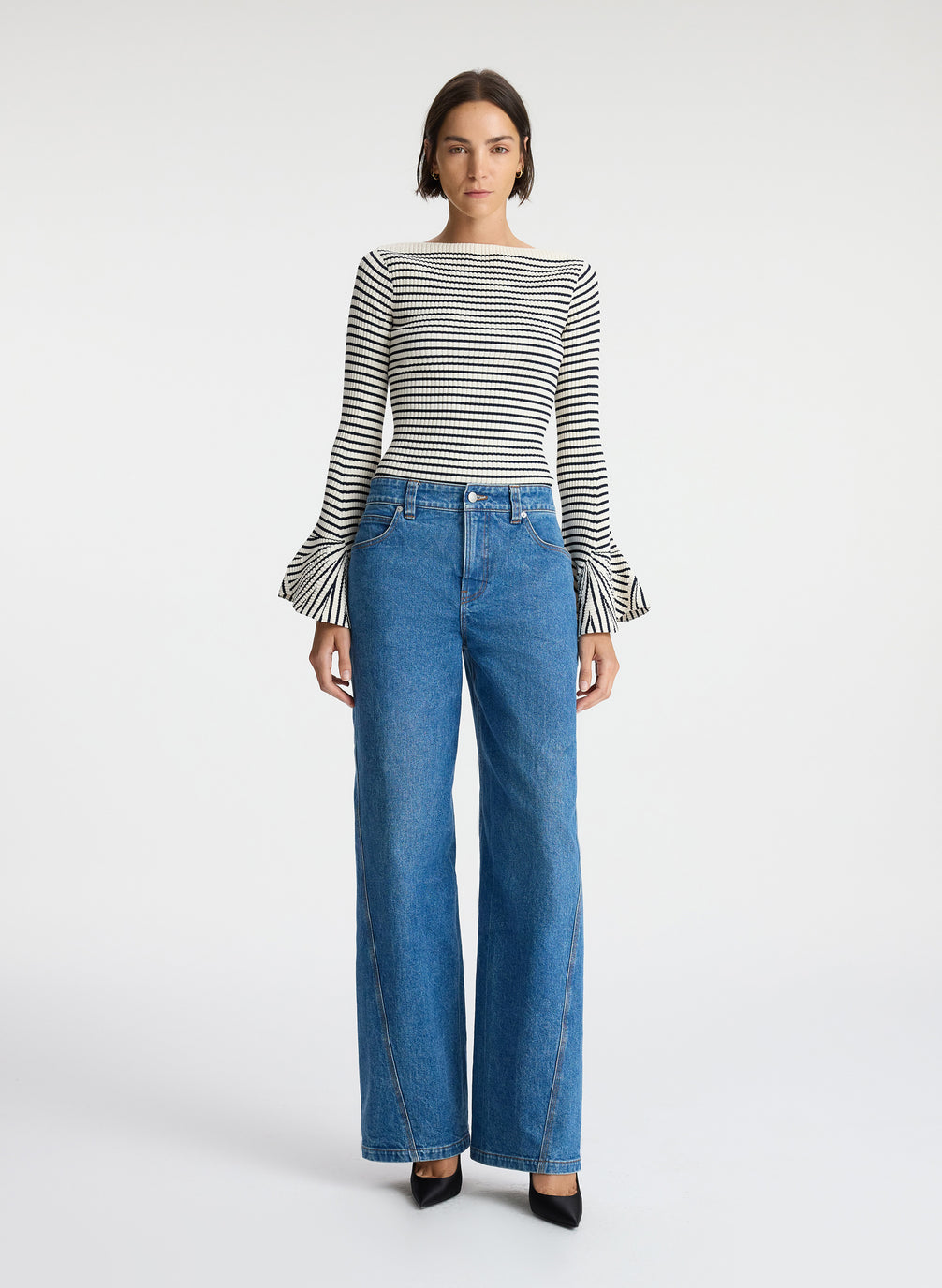 front view of woman wearing striped long bell sleeve knit top and medium blue wash denim jeans