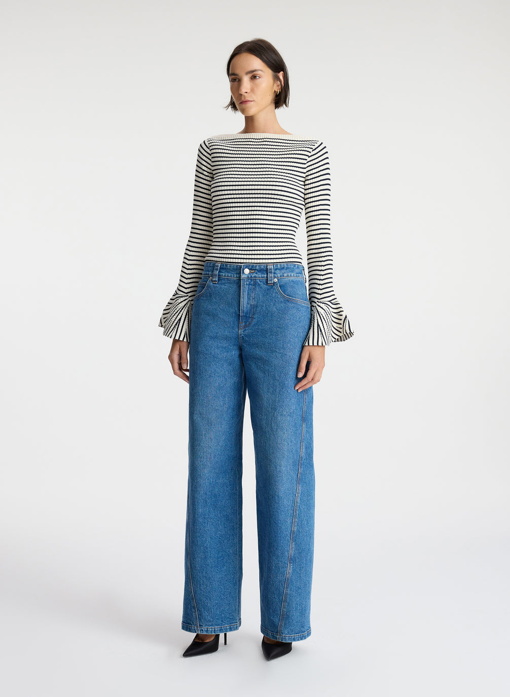 side view of woman wearing striped long bell sleeve knit top and medium blue wash denim jeans
