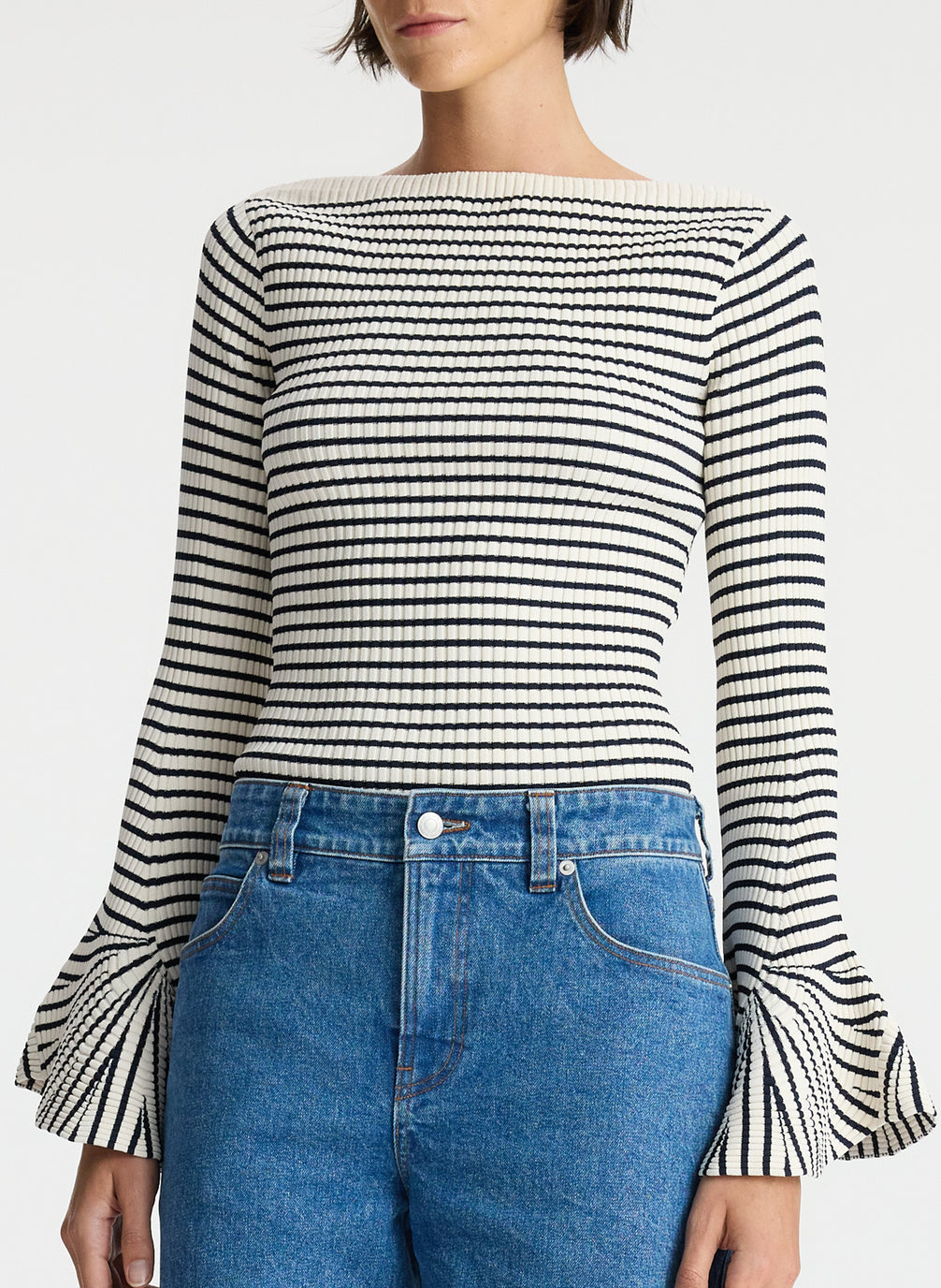 front view of woman wearing striped long bell sleeve knit top and medium blue wash denim jeans
