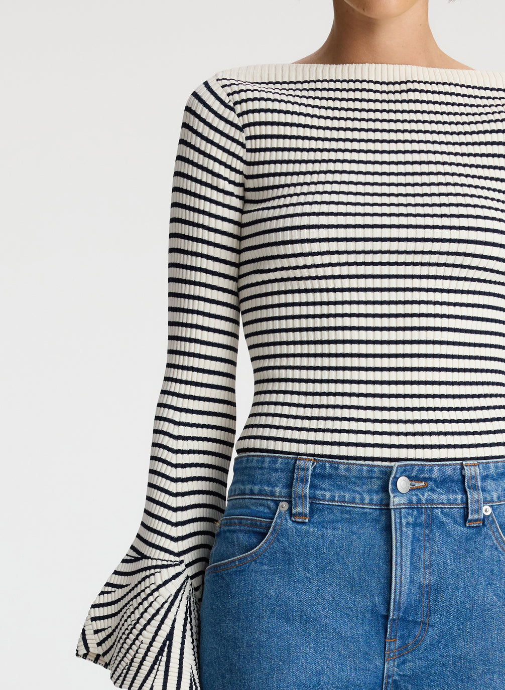 detail view of woman wearing striped long bell sleeve knit top and medium blue wash denim jeans
