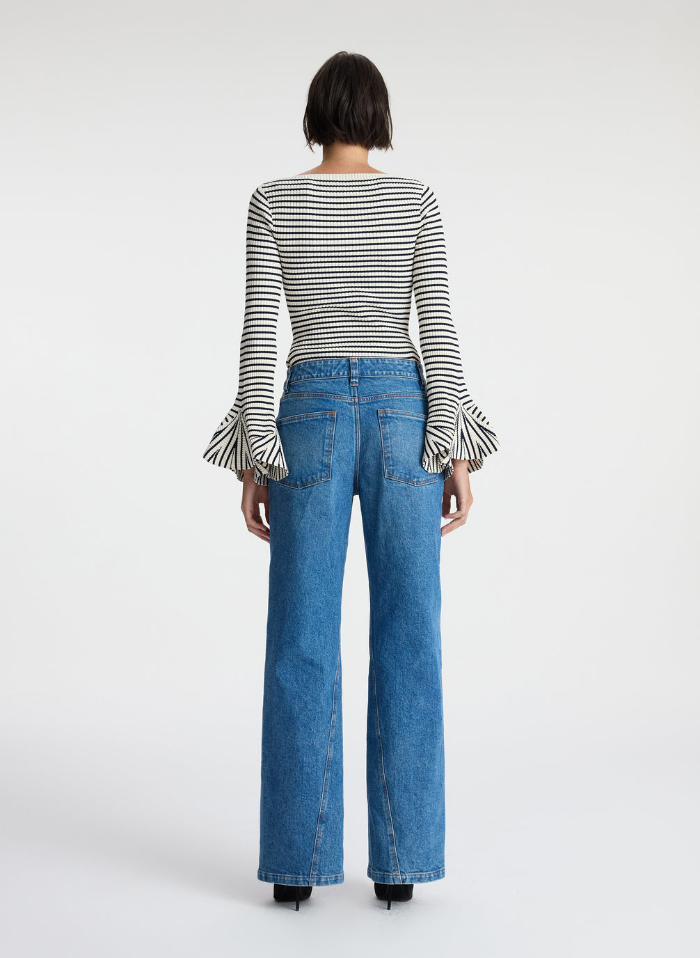 back view of woman wearing striped long bell sleeve knit top and medium blue wash denim jeans