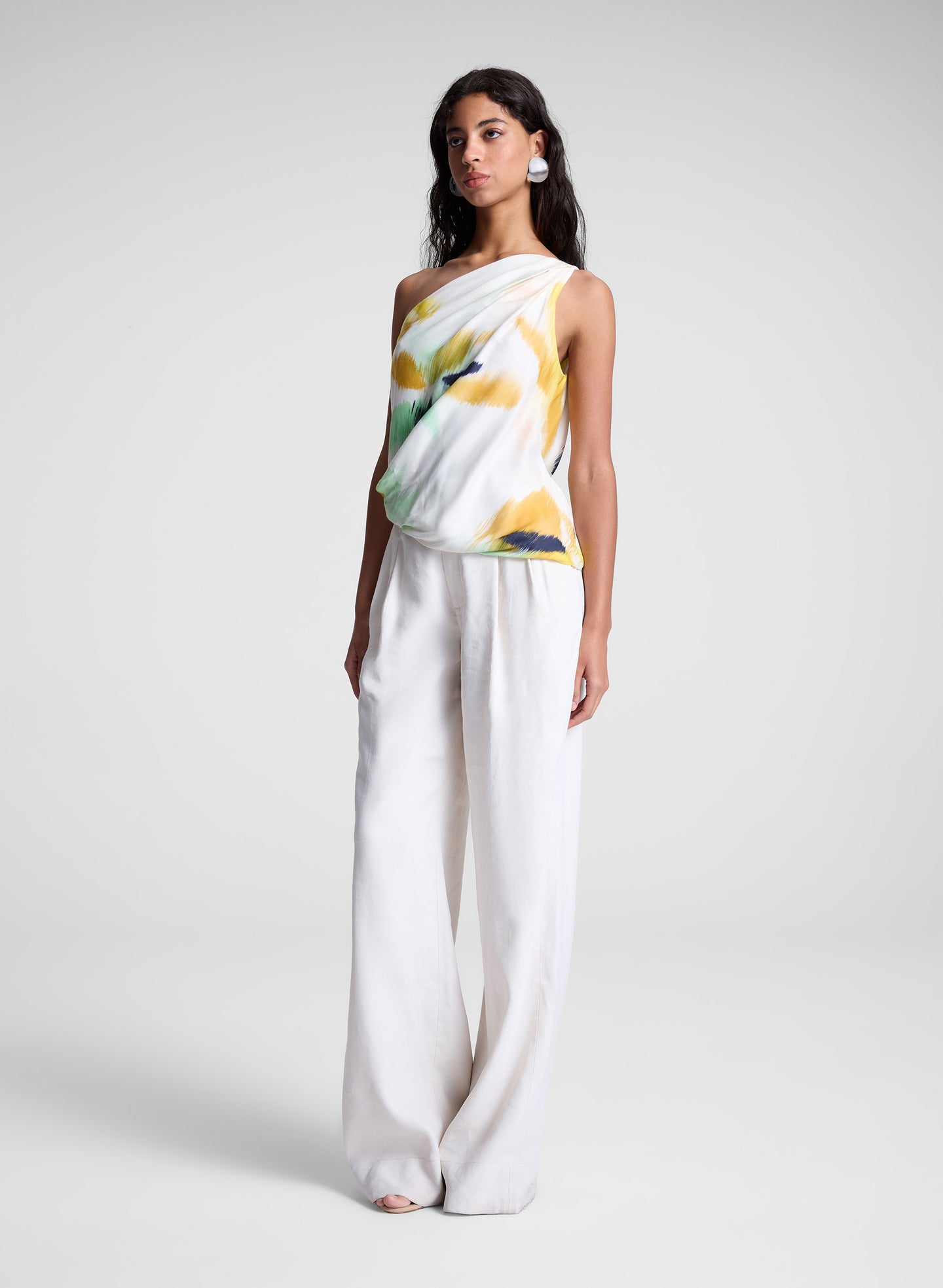woman wearing one shoulder printed top and cream wide leg pants