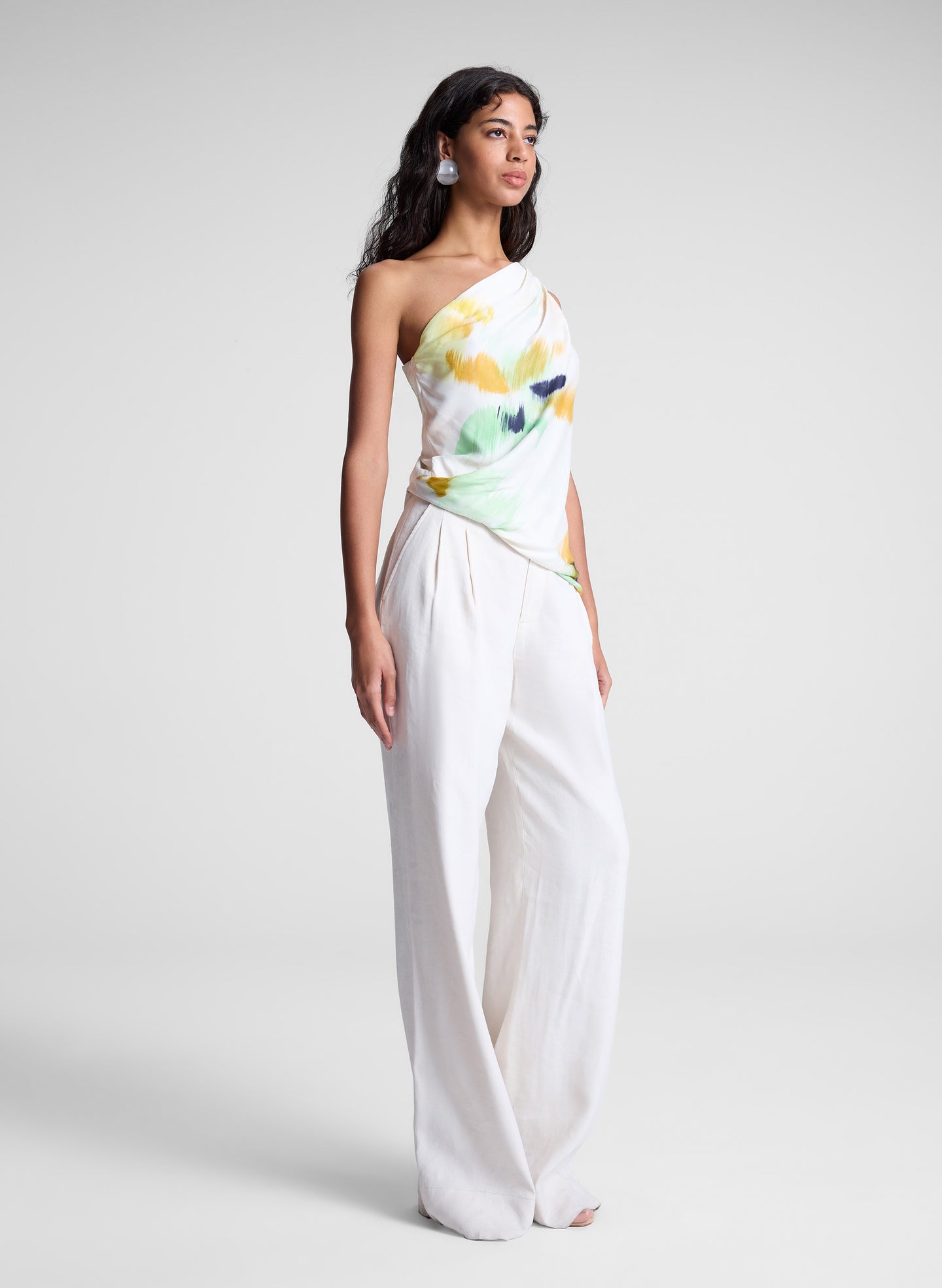 woman wearing one shoulder printed top and cream wide leg pants