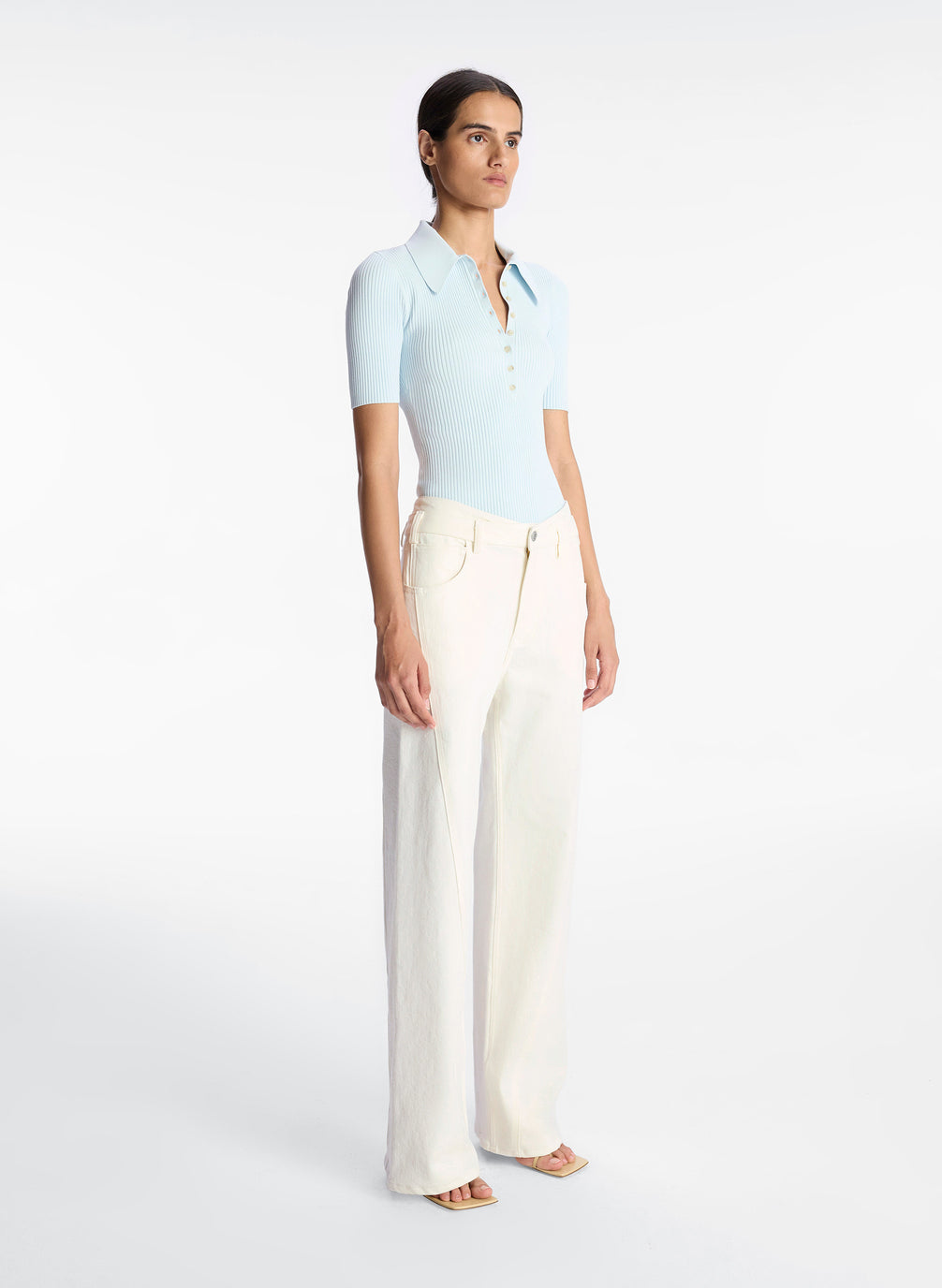 side view of woman wearing light blue collared shirt and white wide leg jeans