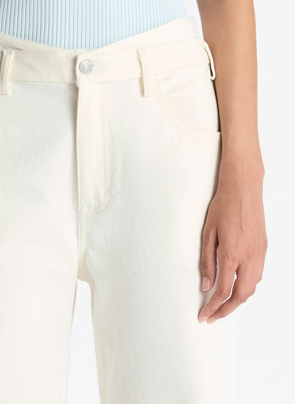 detail view of woman wearing light blue collared shirt and white wide leg jeans