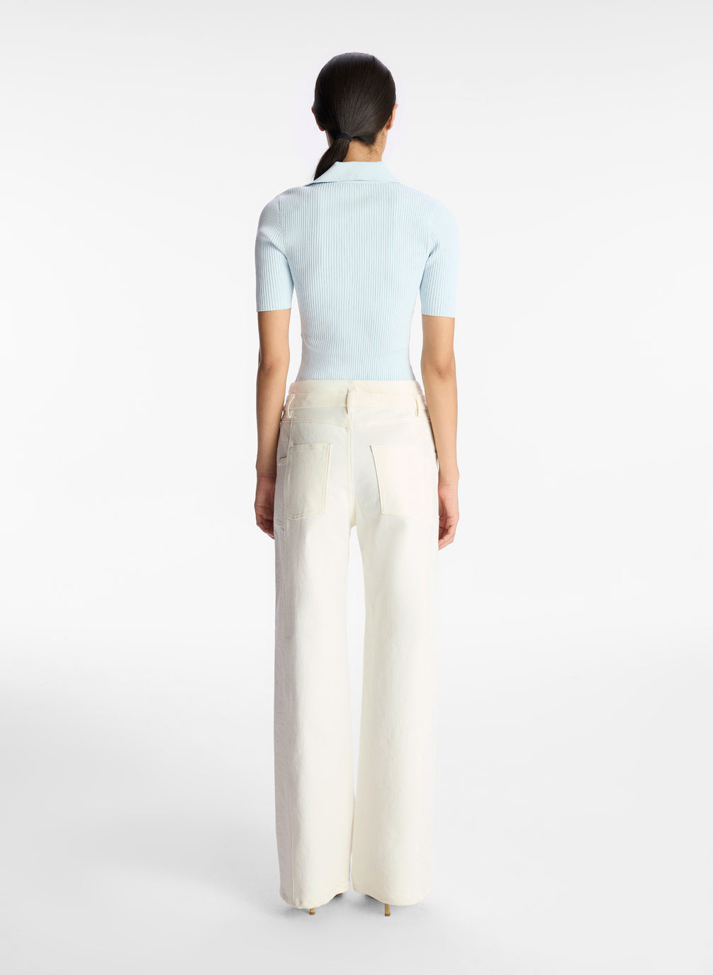 back view of woman wearing light blue collared shirt and white wide leg jeans
