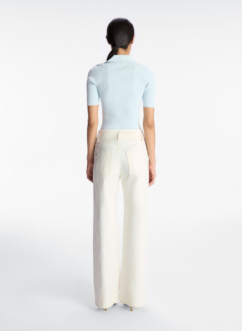 back view of woman wearing light blue short sleeve knit collared top and white denim pants