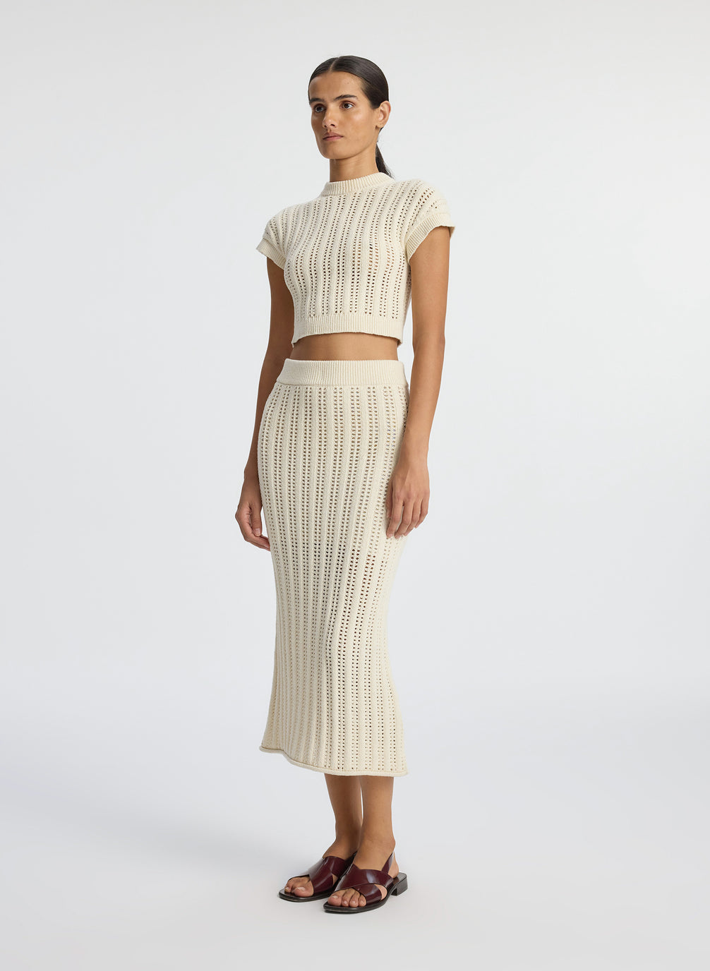side view of woman wearing cream open weave cropped top and and matching midi skirt