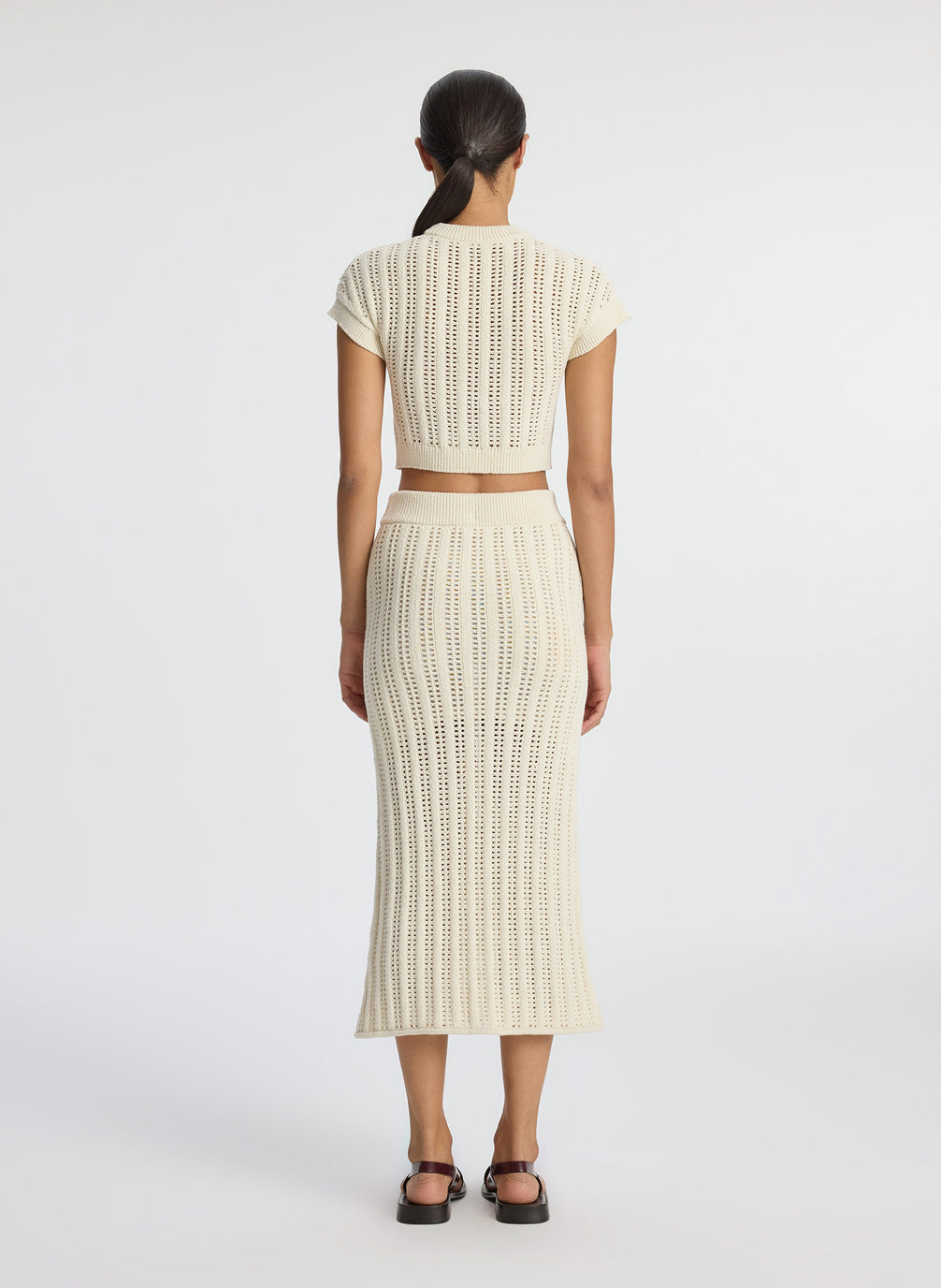 back view of woman wearing cream open weave cropped top and and matching midi skirt