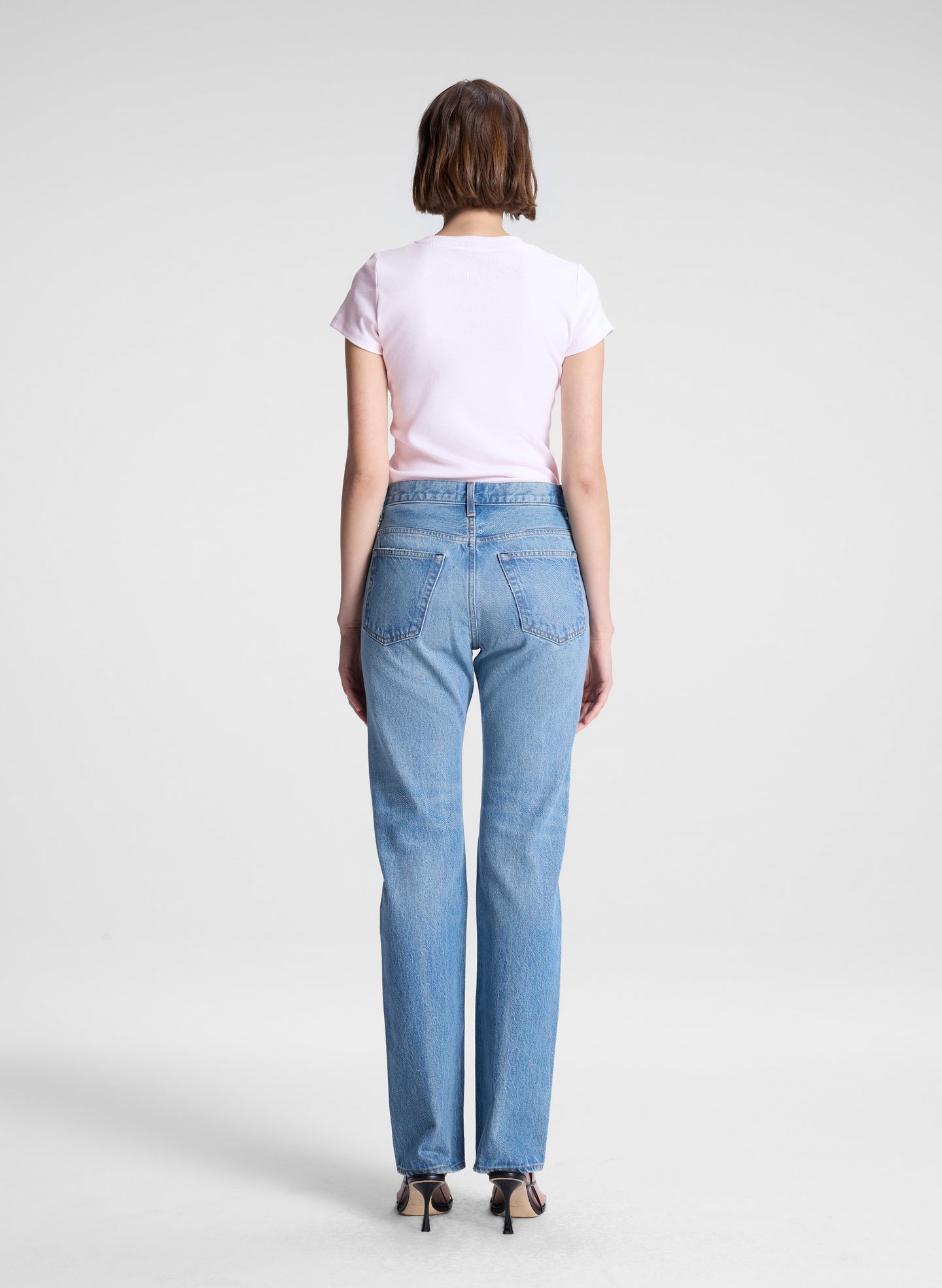 woman wearing light pink tee and light blue wash denim straight leg jeans