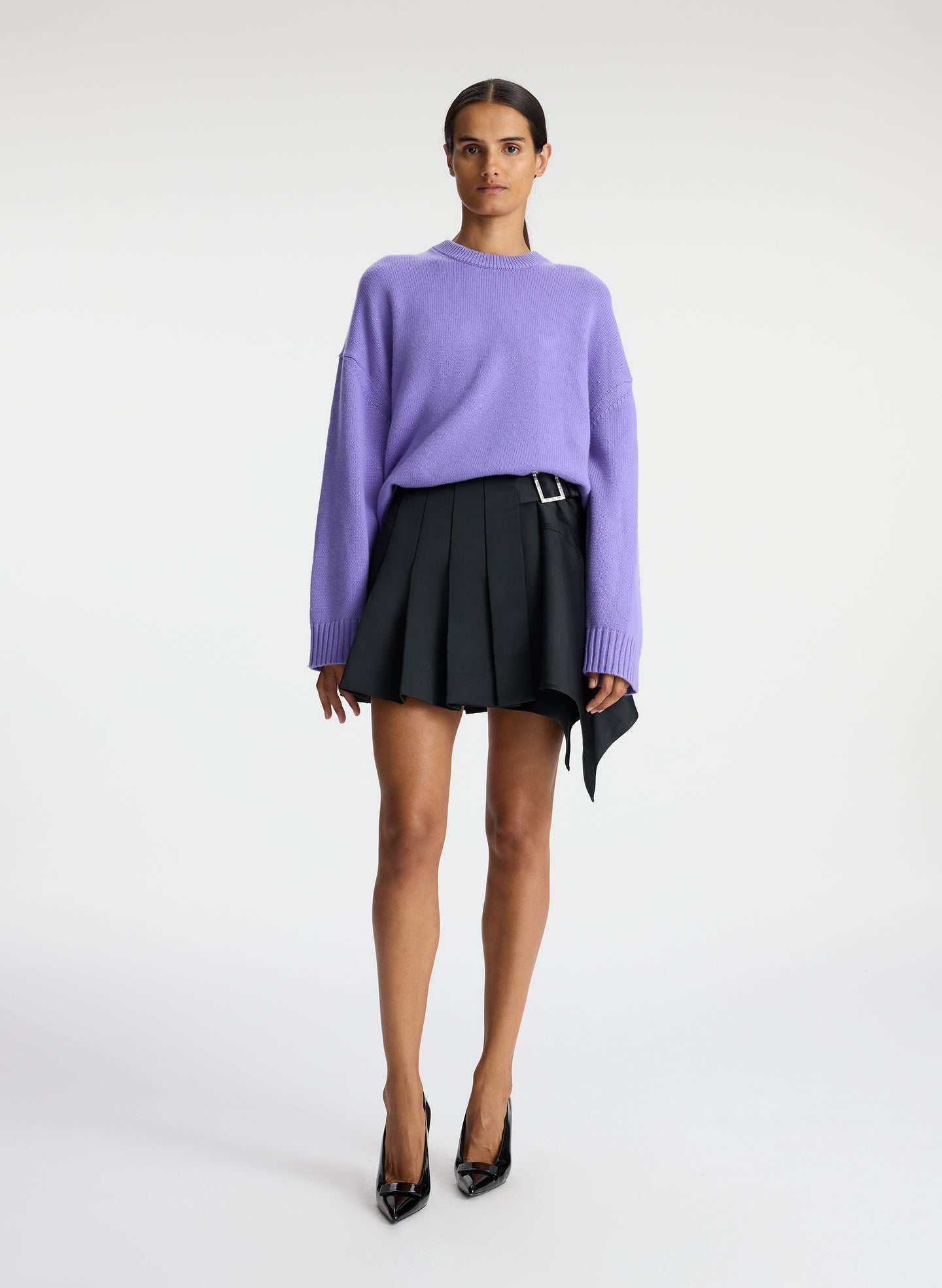 front view of woman wearing purple sweater and black pleated mini skirt