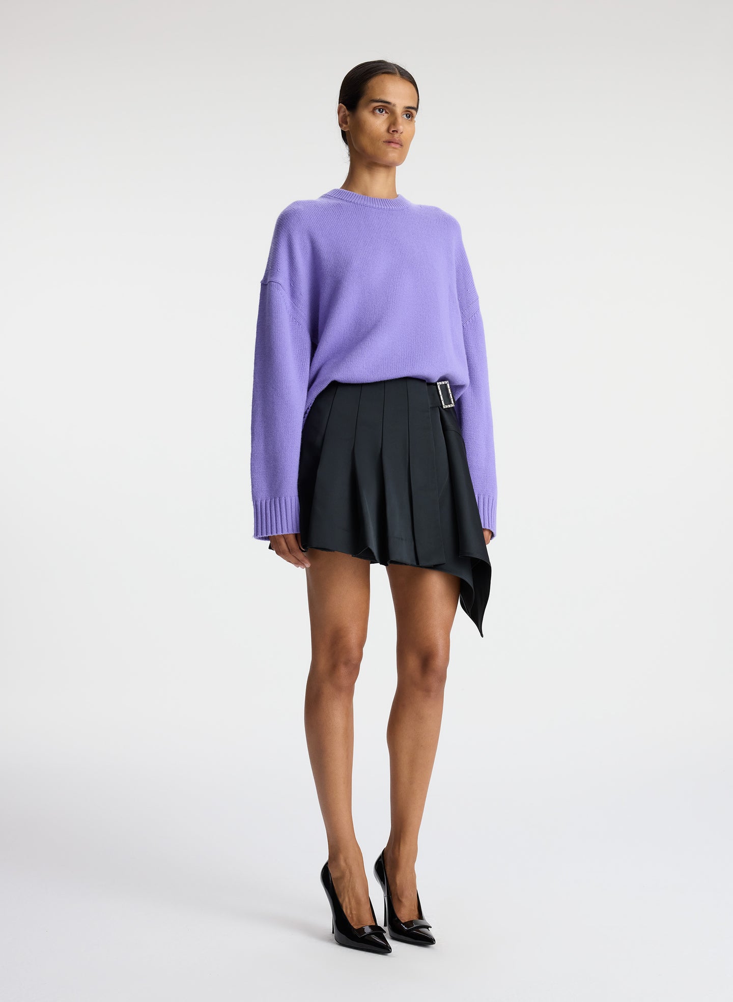 side view of woman wearing purple sweater and black pleated mini skirt