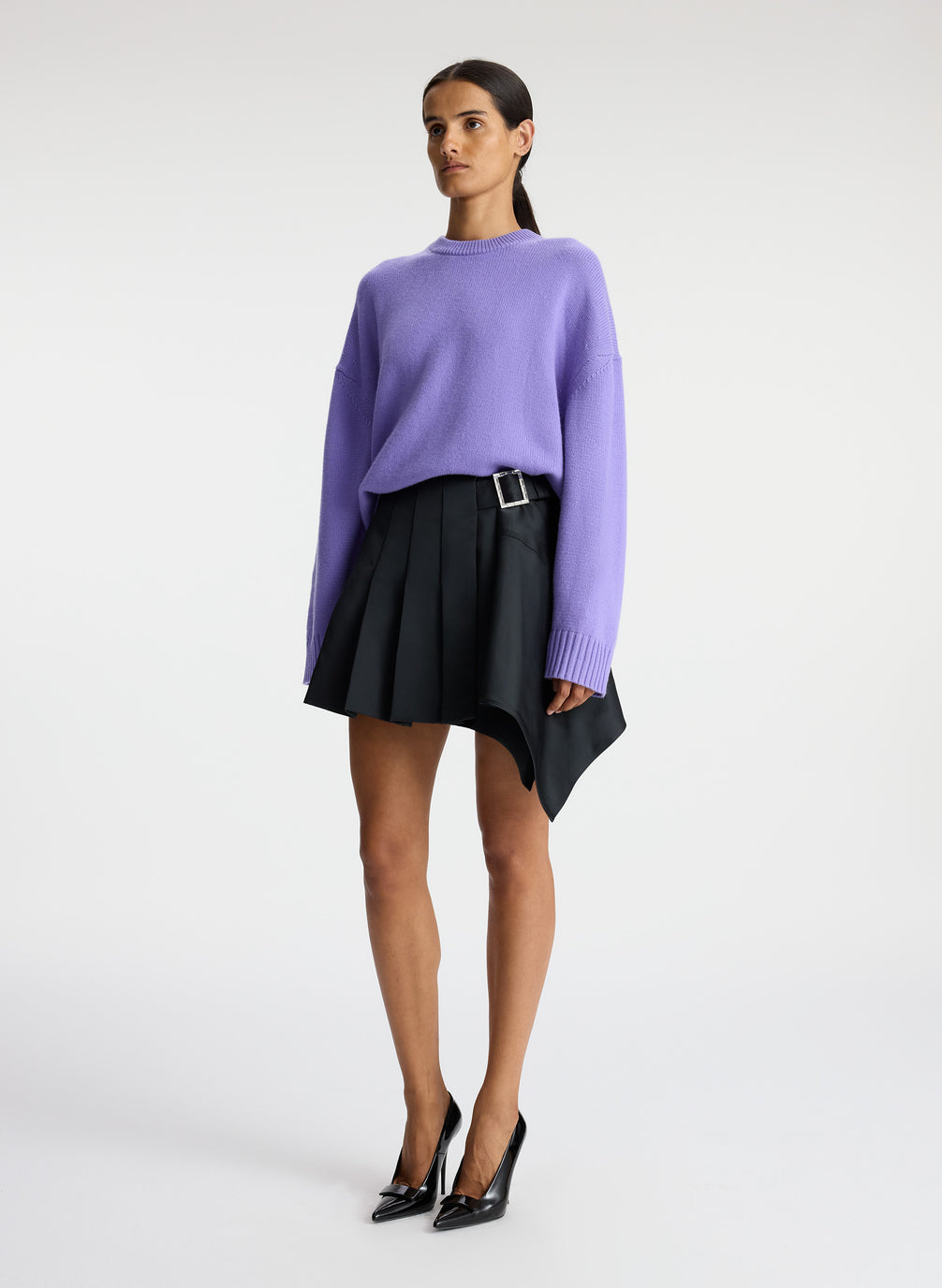 side view of woman wearing purple sweater and black pleated mini skirt
