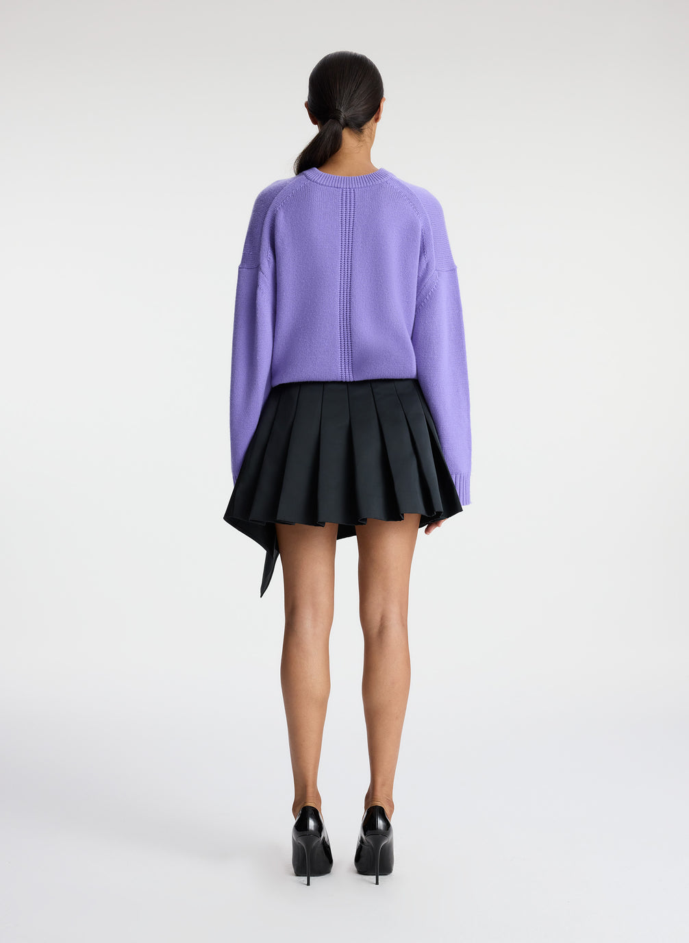 back view of woman wearing purple sweater and black pleated mini skirt