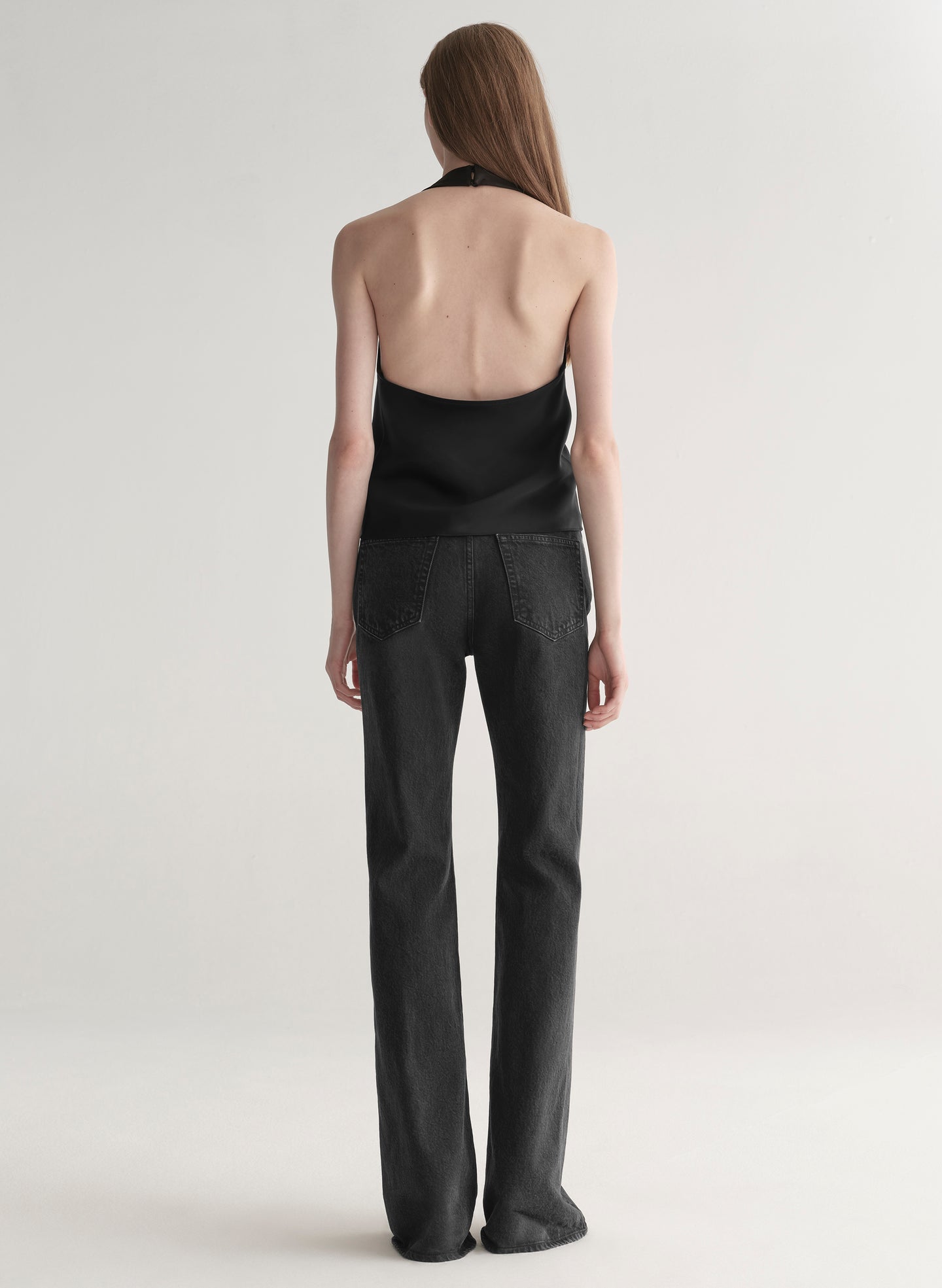 Woman wearing a black sleeveless top and black denim jeans on a plain background