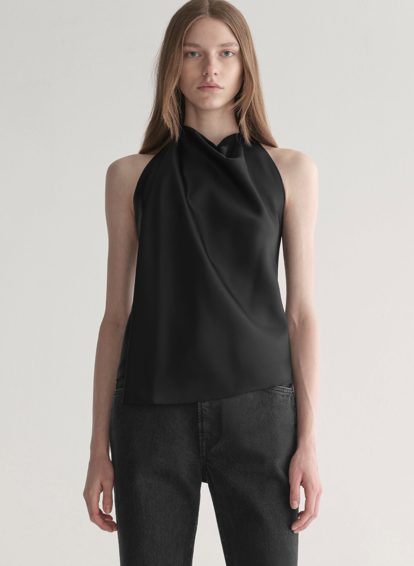 Woman wearing a black sleeveless top and black denim jeans on a plain background