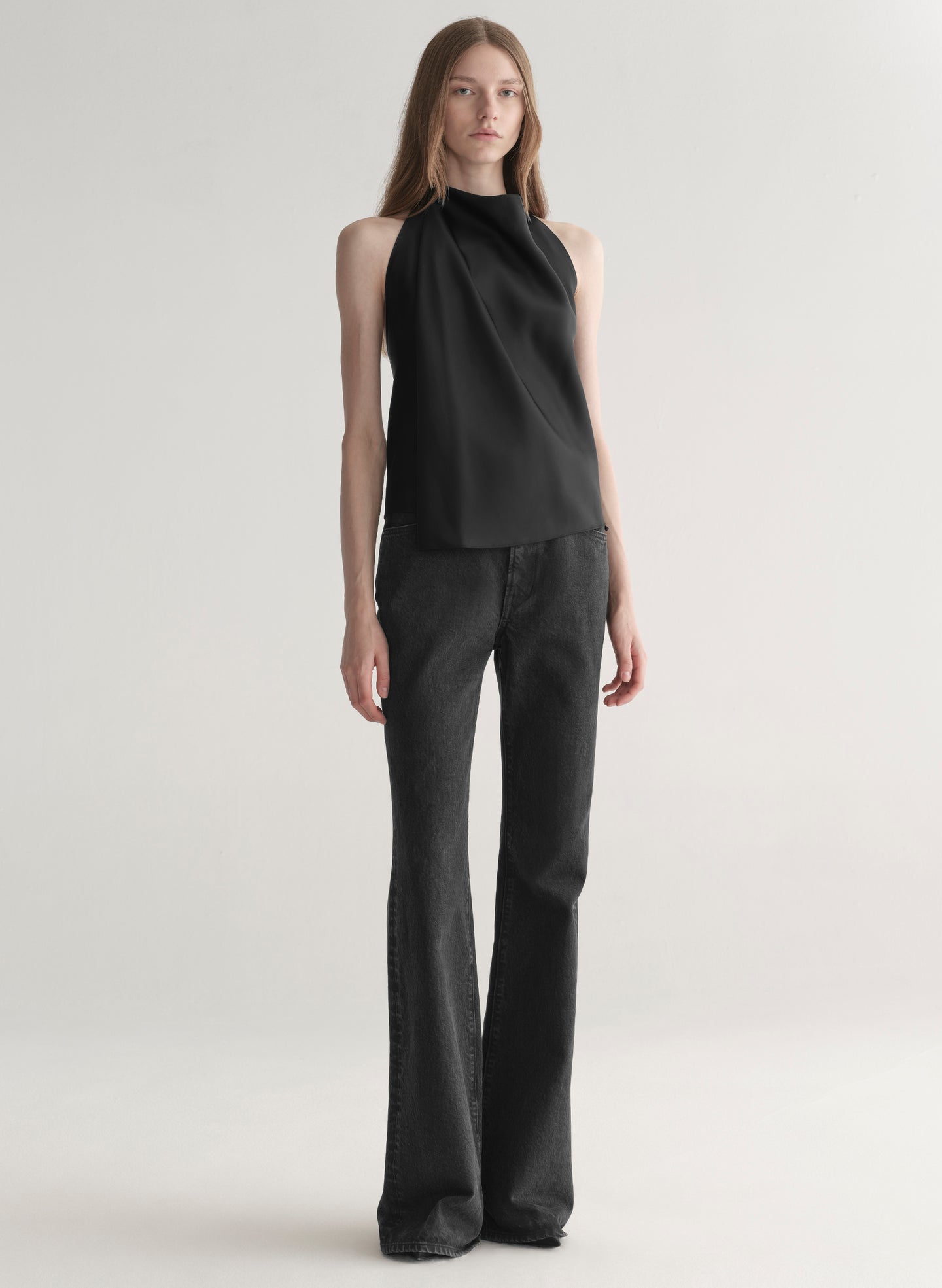 Woman wearing a black sleeveless top and black denim jeans on a plain background