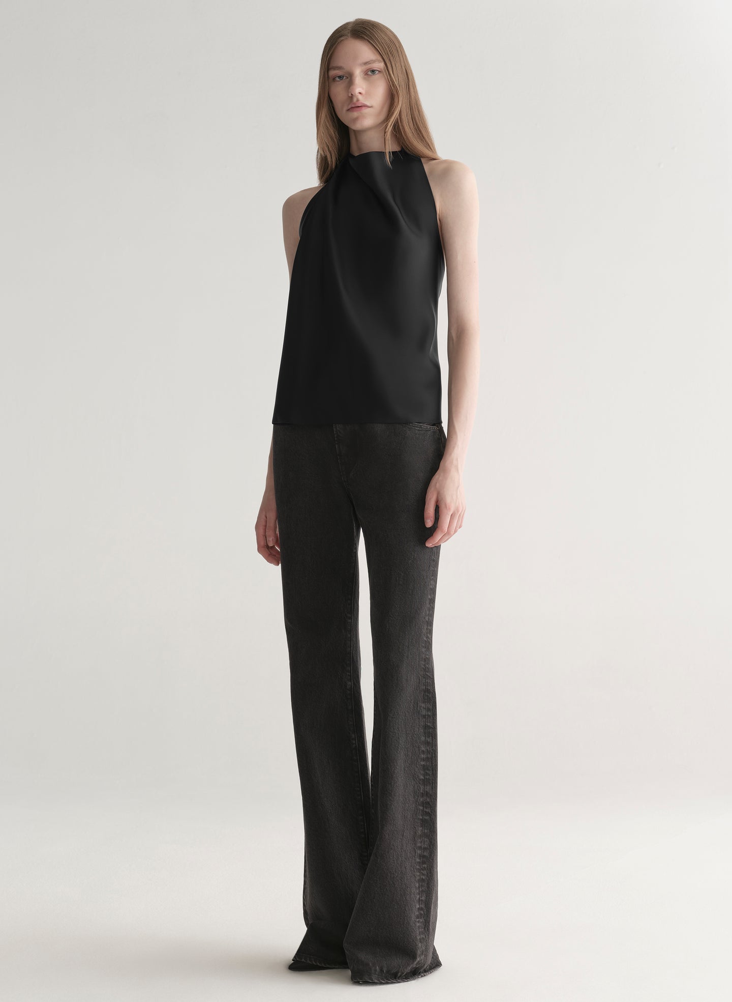 Woman wearing a black sleeveless top and black denim jeans on a plain background