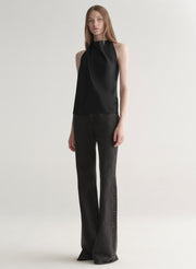 Woman wearing a black sleeveless top and black denim jeans on a plain background