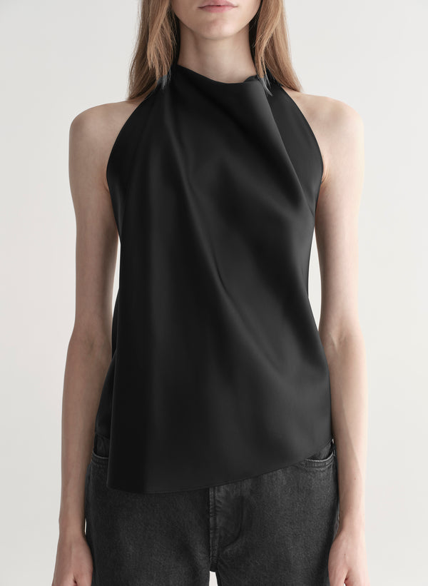 Woman wearing a black sleeveless top and black denim jeans on a plain background