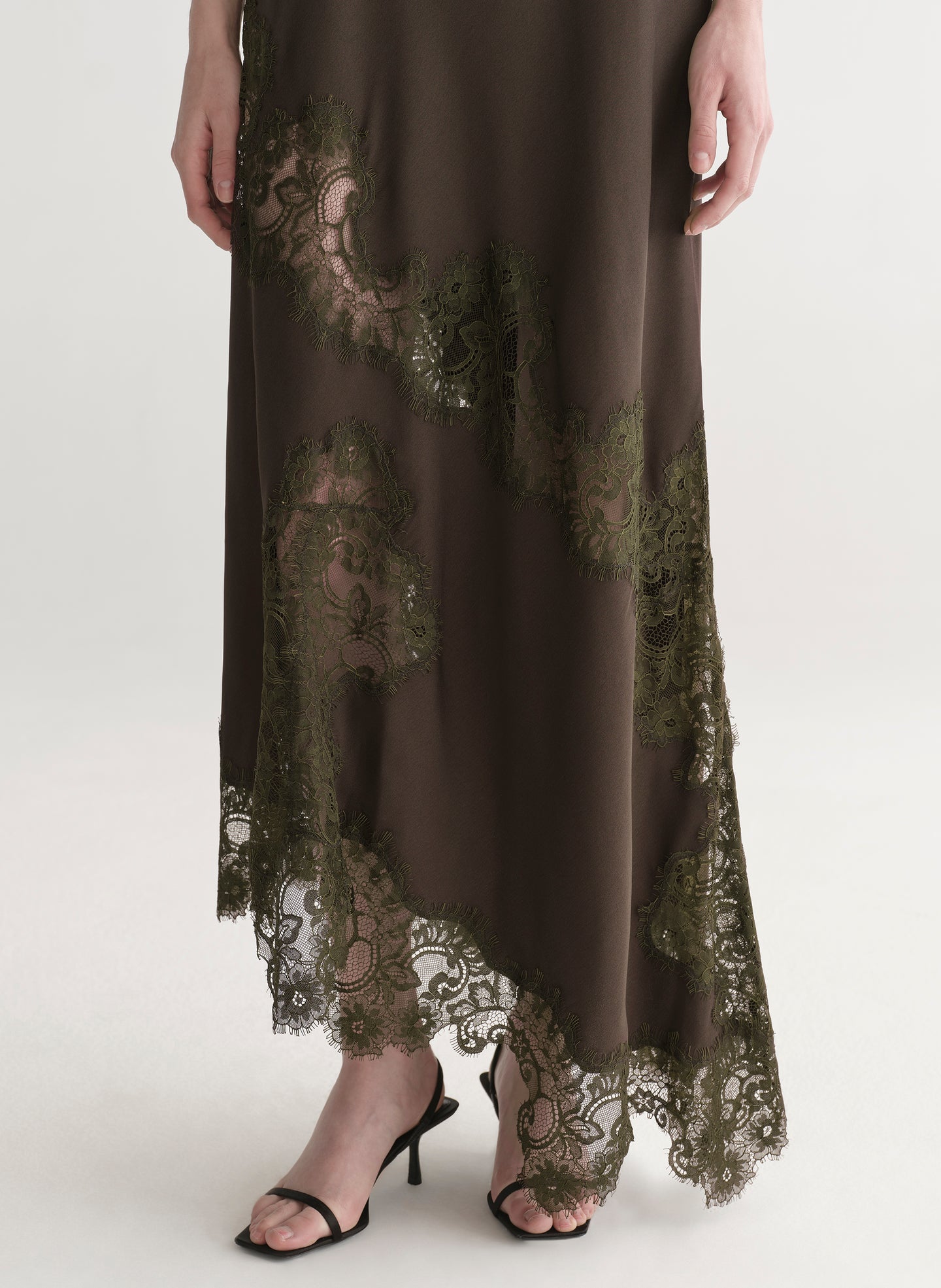 Woman wearing an olive green evening gown with lace details on a white background