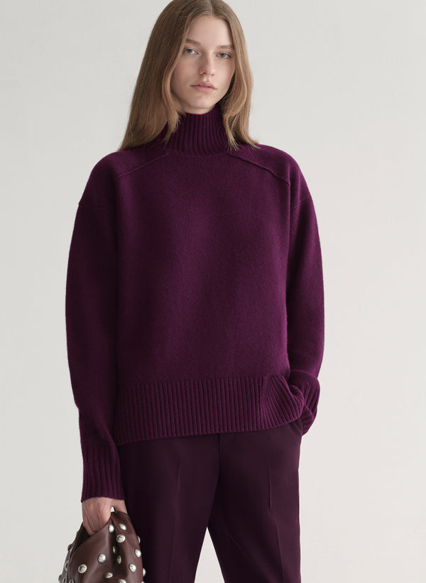 Woman wearing a purple sweater and pants on a light gray background