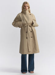 Woman wearing a beige trench coat, white shirt, and blue jeans on a plain background