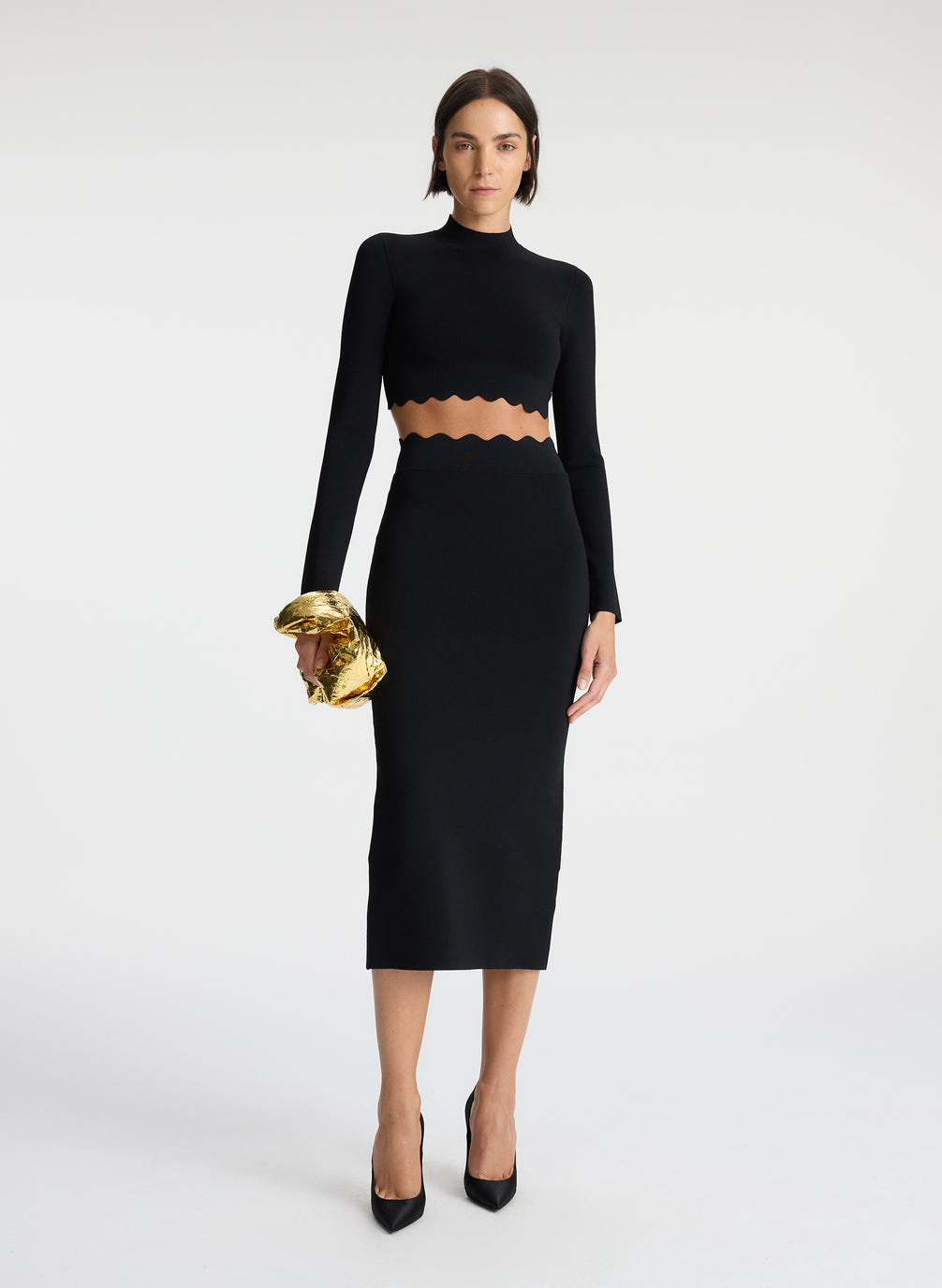 front view of woman wearing black long sleeve crop top  with scallop detailing and matching black scalloped detailing knit midi skirt