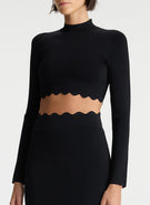 detail view of woman wearing scalloped trim long sleeve black crop top and matching black skirt