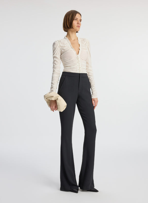 side view of woman wearing white long sleeve v neck top and black flared pants