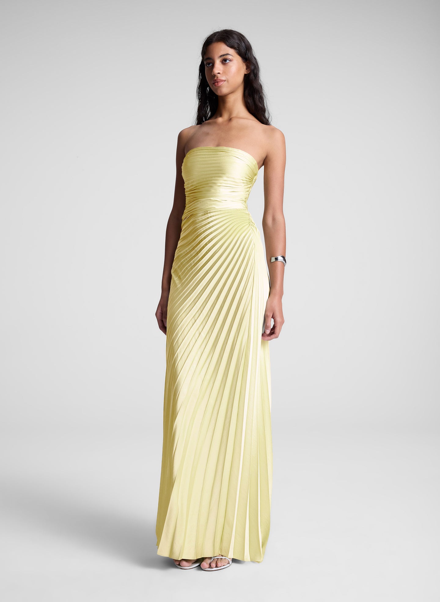Woman wearing a strapless, light yellow evening gown on a plain background